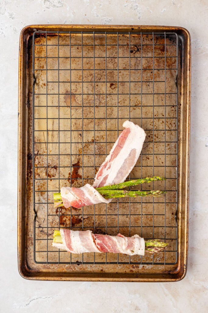 Sheet pan with a cooling rack with bacon wrapped asparagus, being assembled