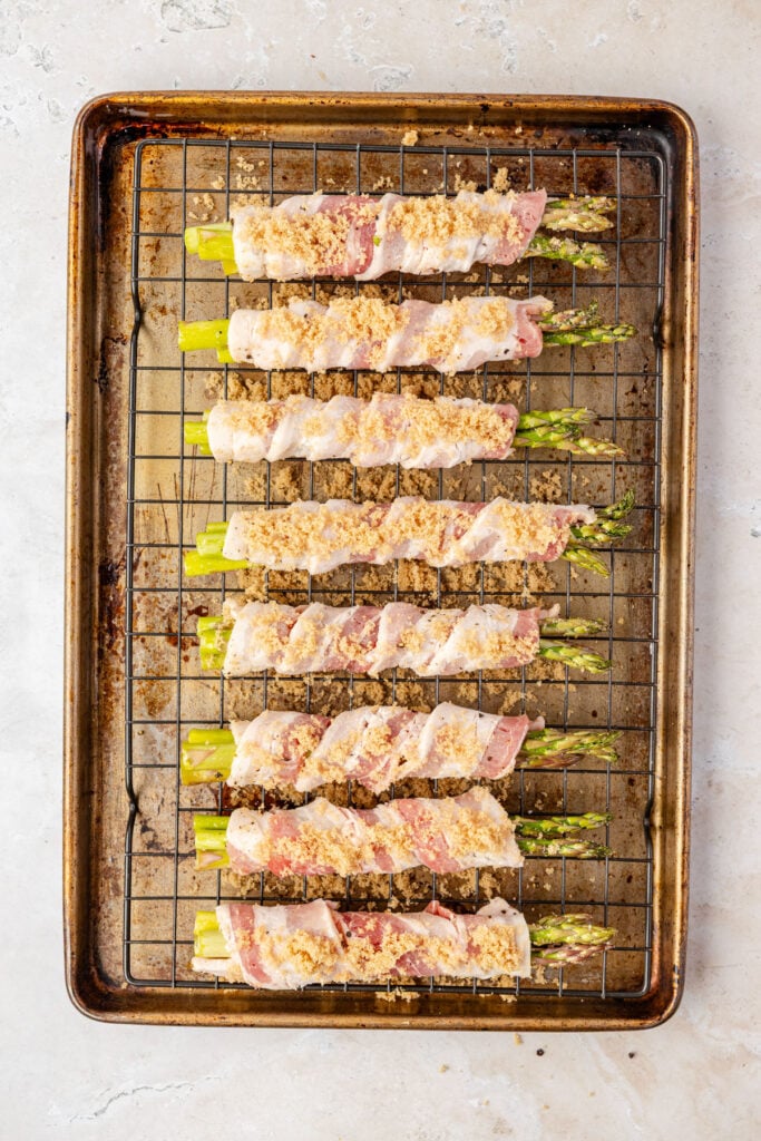 Sheet pan of raw bacon wrapped asparagus on a cooling rack