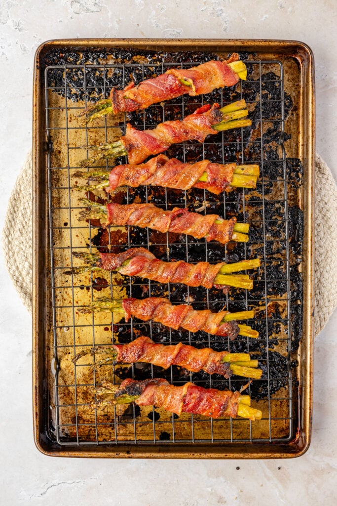 Cooked bacon wrap, asparagus on a cooling rack on top of the sheet pan