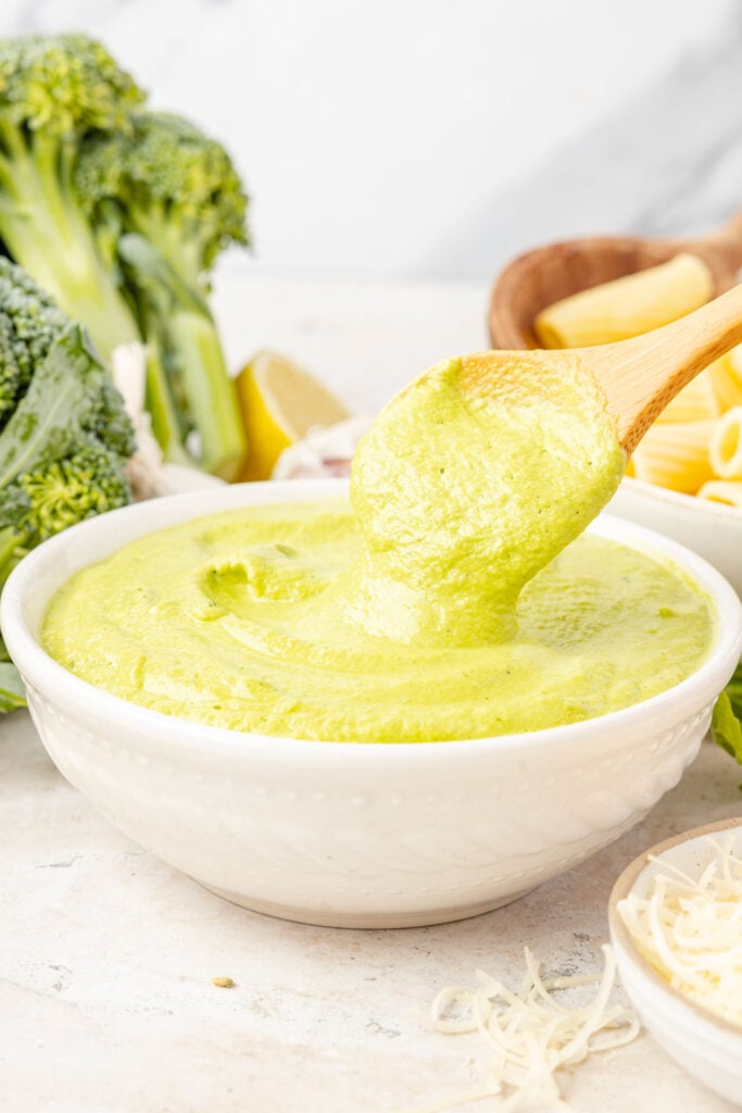 Broccoli pesto in a bowl with broccoli pesto in a bowl behind it with broccoli and pasta in the background