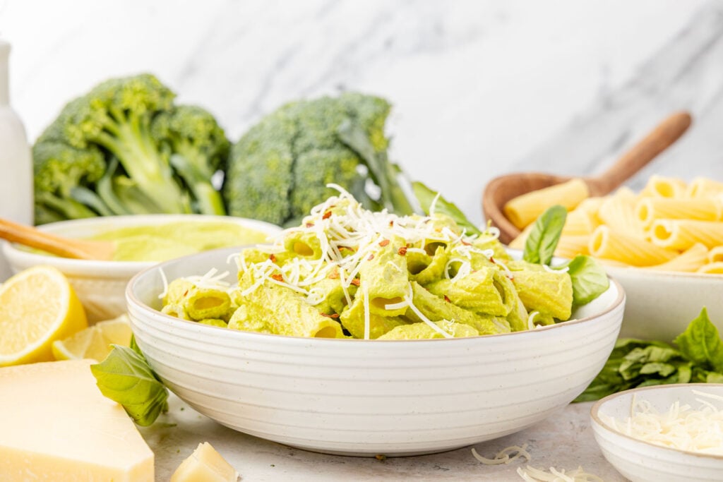 Broccoli pesto over pasta enable with broccoli pesto in a bowl behind it with broccoli and pasta in the background