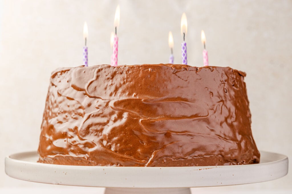 Homemade Chocolate Frosting on an angel food cake on a cake stand with birthday candles