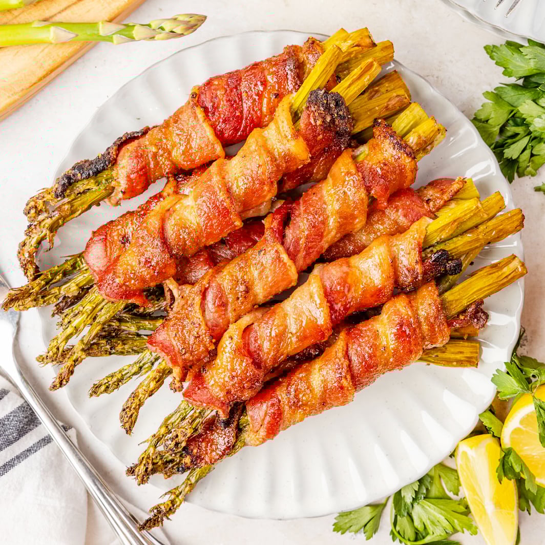 A plate of bacon wrapped asparagus with parsley and lemons around it