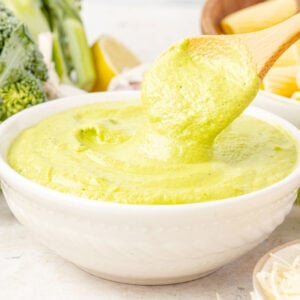 Broccoli pesto in a bowl with broccoli pesto in a bowl behind it with broccoli and pasta in the background