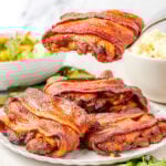 Bacon wrapped chicken thighs on a plate with a serving utensil scooping up one chicken thigh