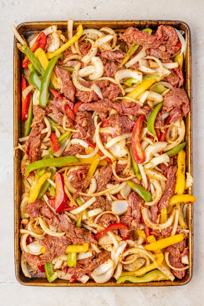 Raw seasoned steak, peppers, and onions on a sheet pan for sheet pan steak fajitas