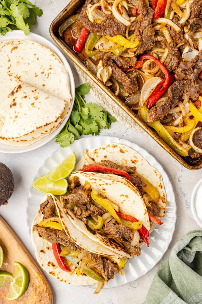 Cheap pan steak fajitas, a plate of tortillas and a plate of prepared fajitas with lime wedges