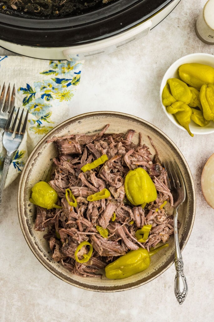 Close up of juicy slow cooker Italian beef with pepperoncini peppers in a bowl