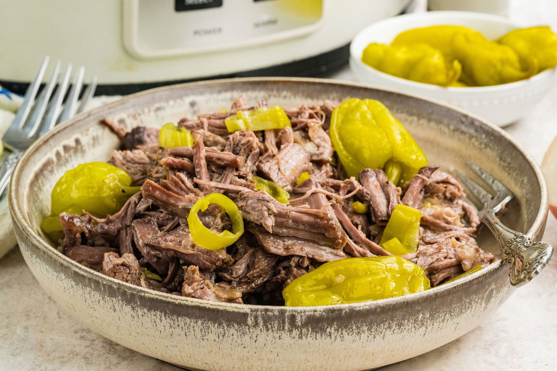 Close up of juicy slow cooker Italian beef with pepperoncini peppers in a bowl