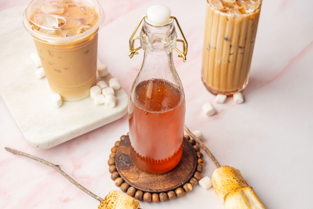 Toasted Marshmallow Syrup in a bottle with two iced coffees in the background