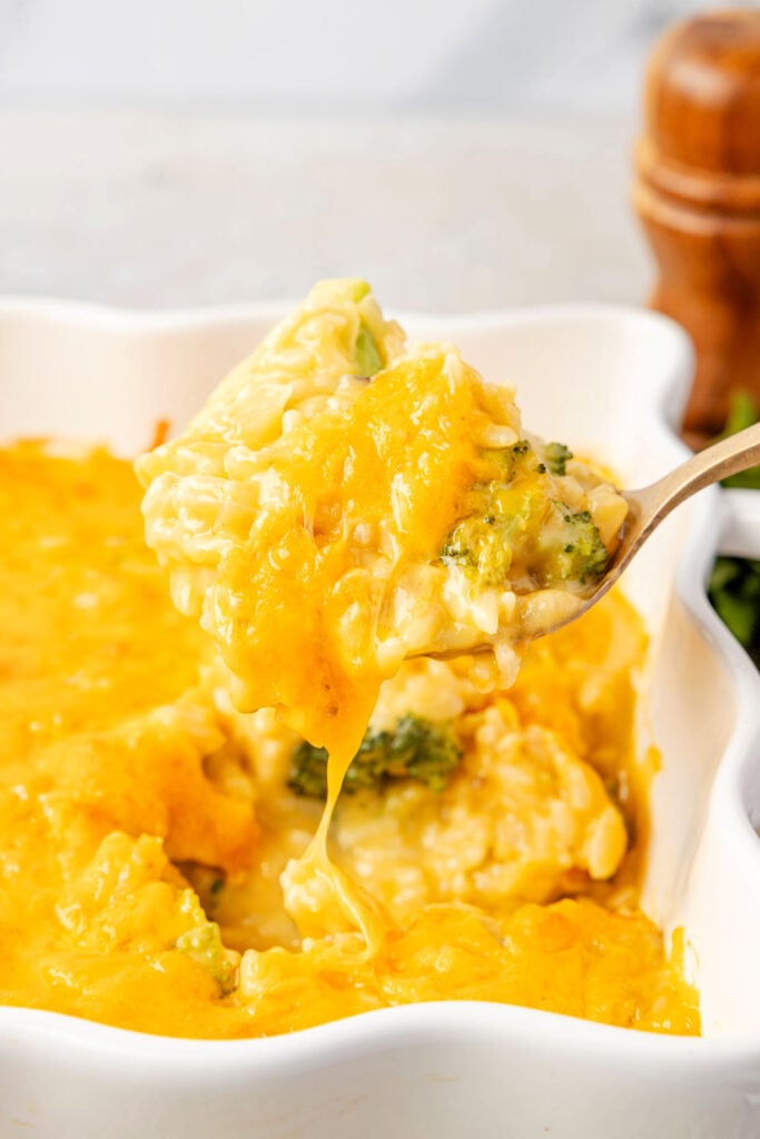 Scooping up broccoli rice casserole out of pan with cheese dripping down.