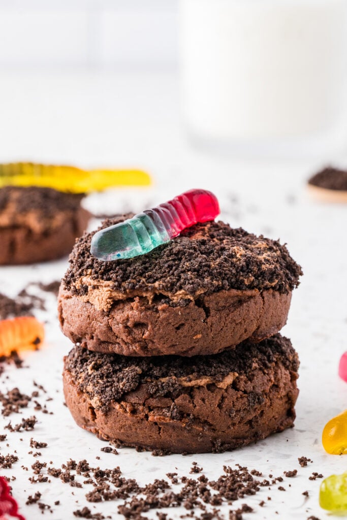 stacked dirt cake cookies, topped with a gummy worm on a white surface with Oreo crumbs around them