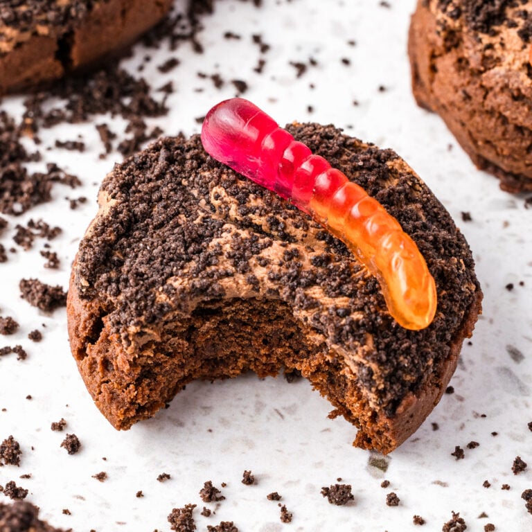 dirt cake cookies, topped with a gummy worm on a white surface with Oreo crumbs around it with a bite taken out of it