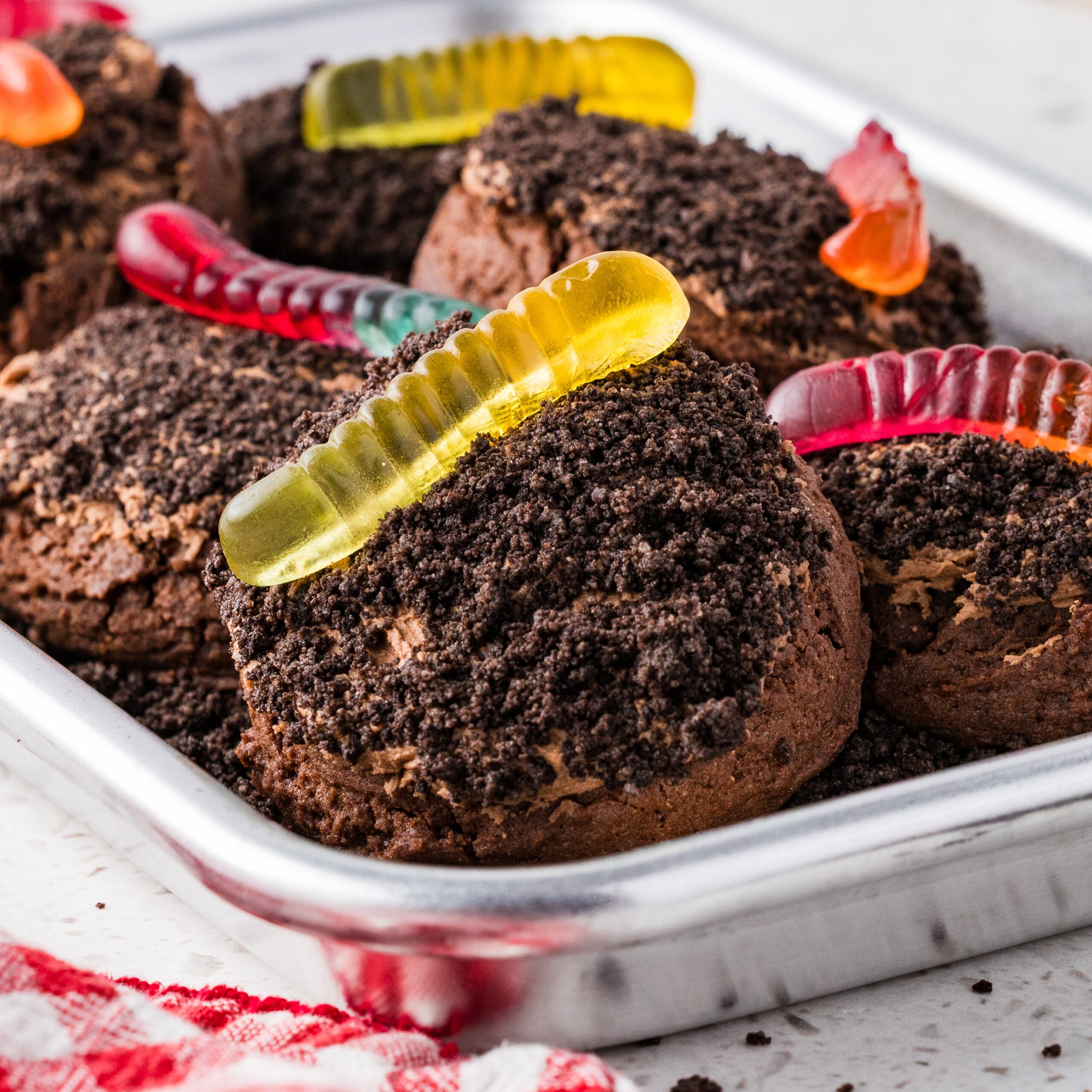 dirt cake cookies, topped with a gummy worm in a silver sheet pan