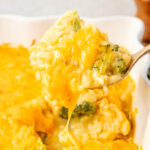 Scooping up broccoli rice casserole out of pan with cheese dripping down.