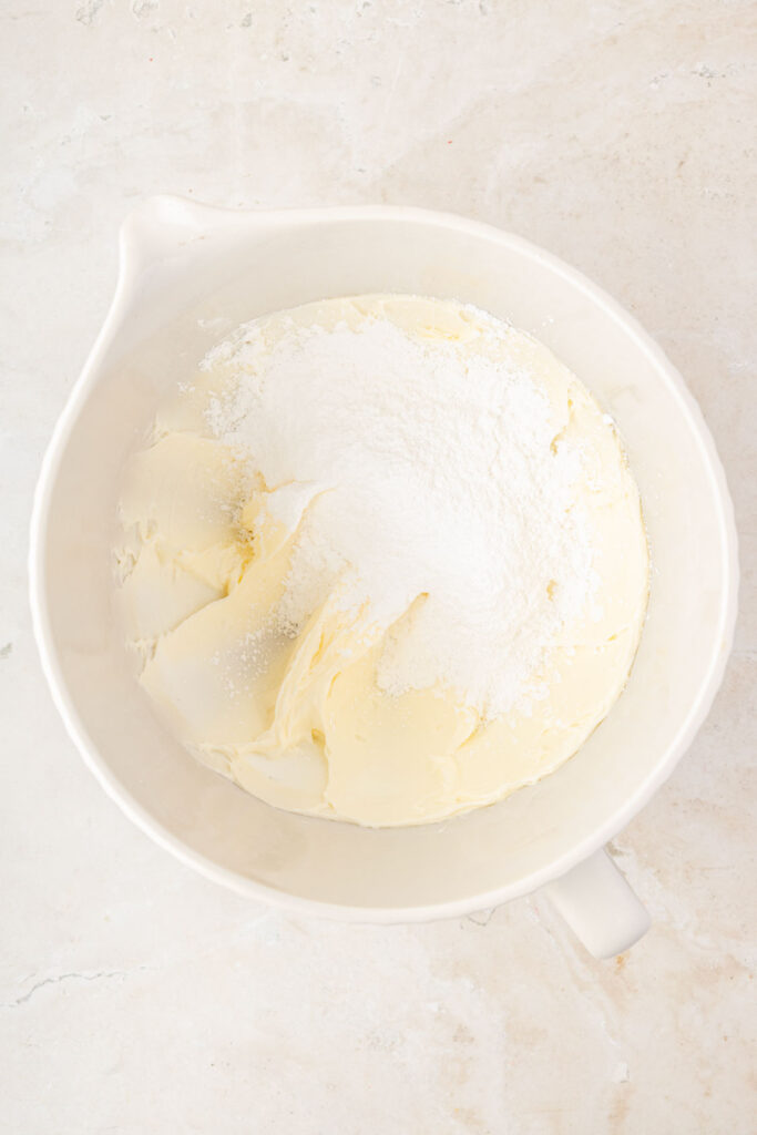 Mixed butter and sugar with powdered sugar shortening, mixed butter and shortening in a mixing bowl with powdered sugar on top.