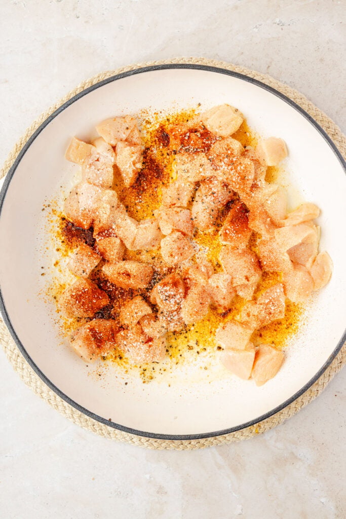 Raw chicken and spices in a pan.