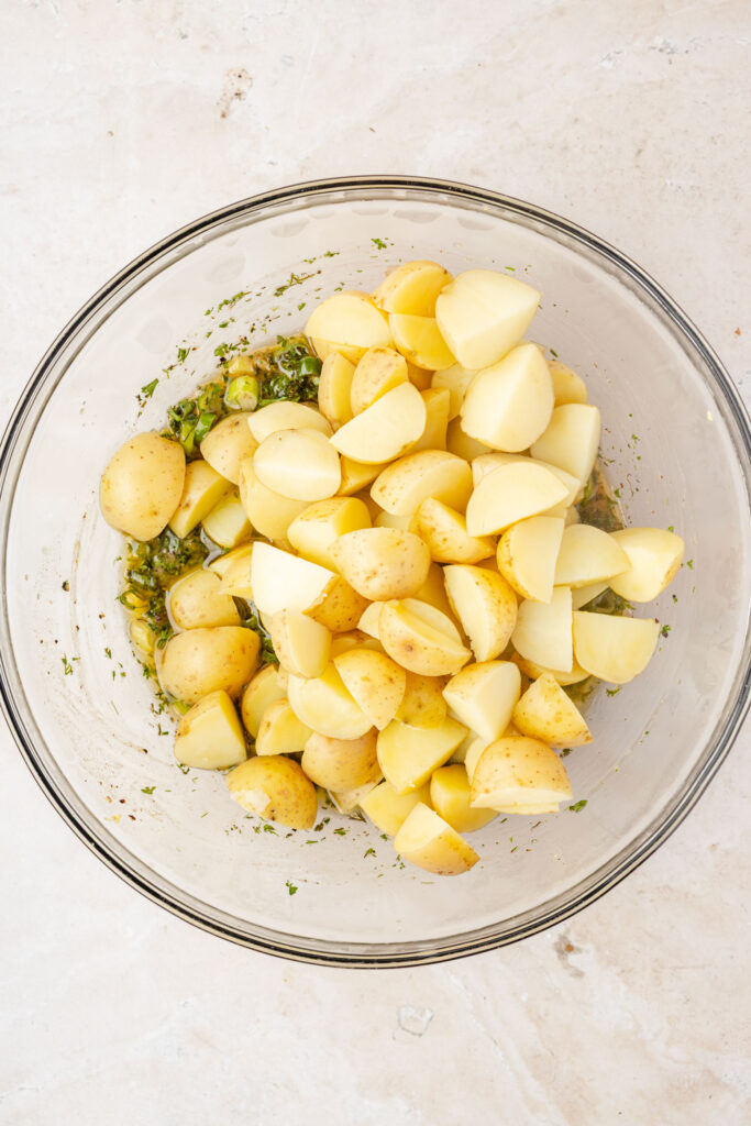 Potatoes and herb vinaigrette in a mixing bowl.