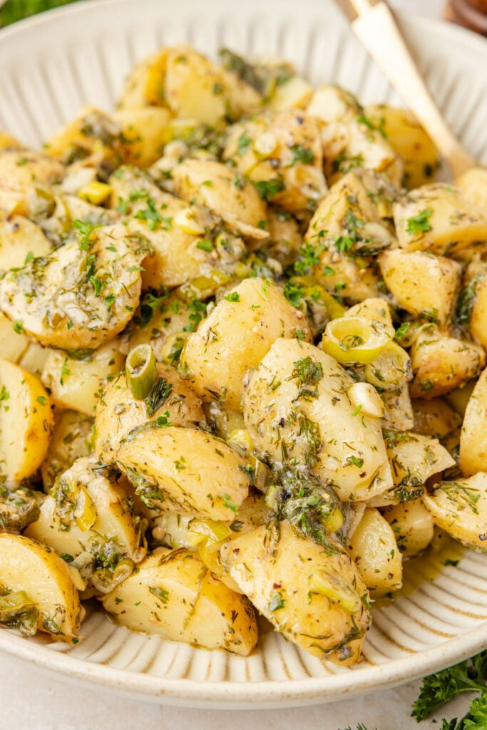 French Potato Salad (Easy No Mayo Potato Salad) in a bowl with herbs around it and a salt and pepper shaker.