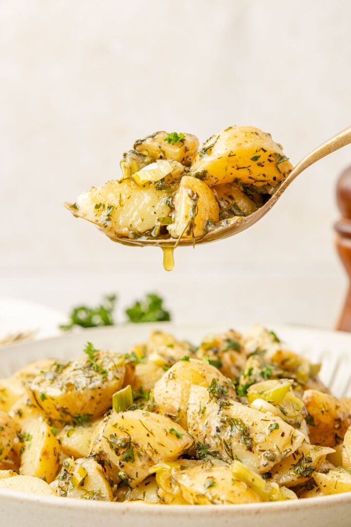 Spoon scooping French Potato Salad (Easy No Mayo Potato Salad) with some dressing dripping off the spoon.