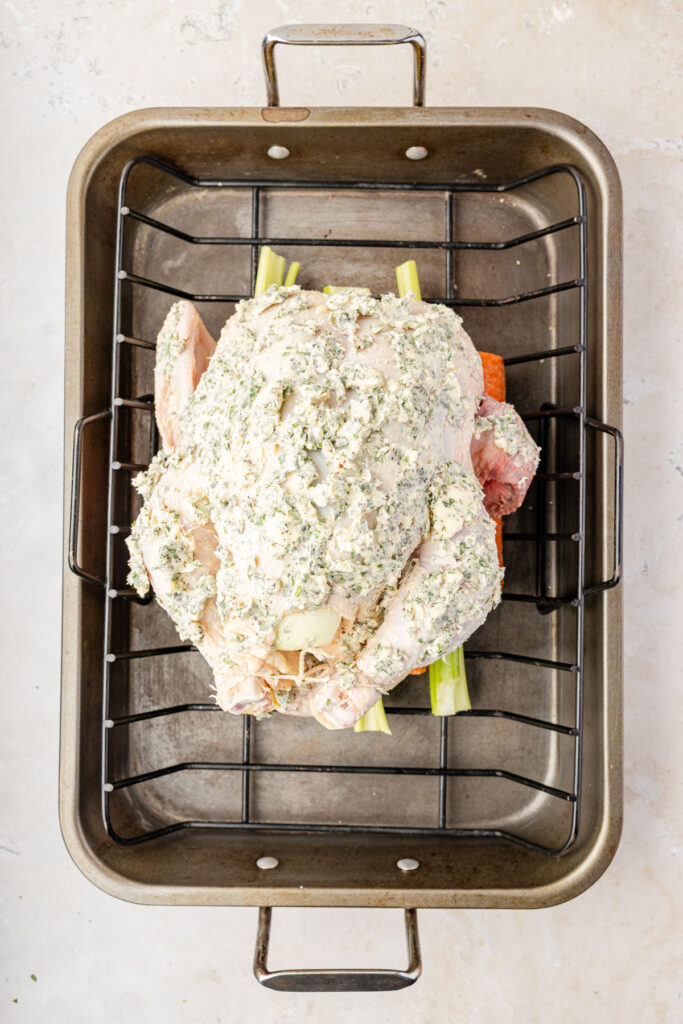 whole chicken coated in garlic herb butter on roasting rack.