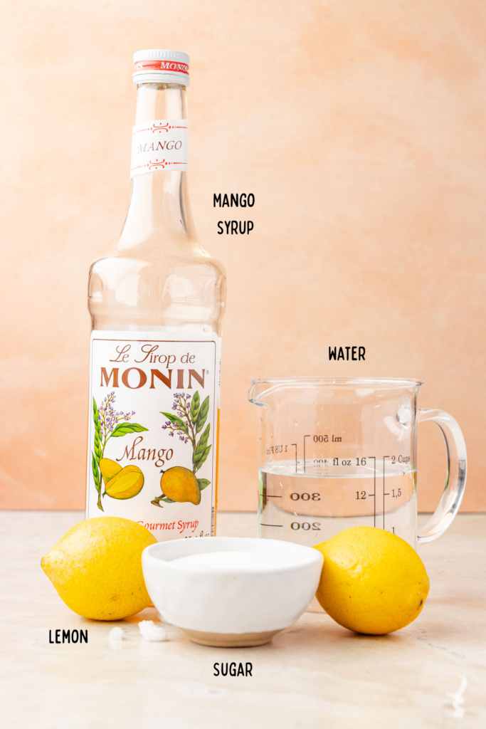 Mango syrup bottle, picture of water, lemons, and sugar in a bowl for mango lemonade