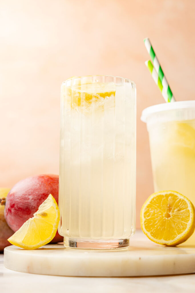 Mango Lemonade in a glass with lemons, inside and lemons and mangoes outside