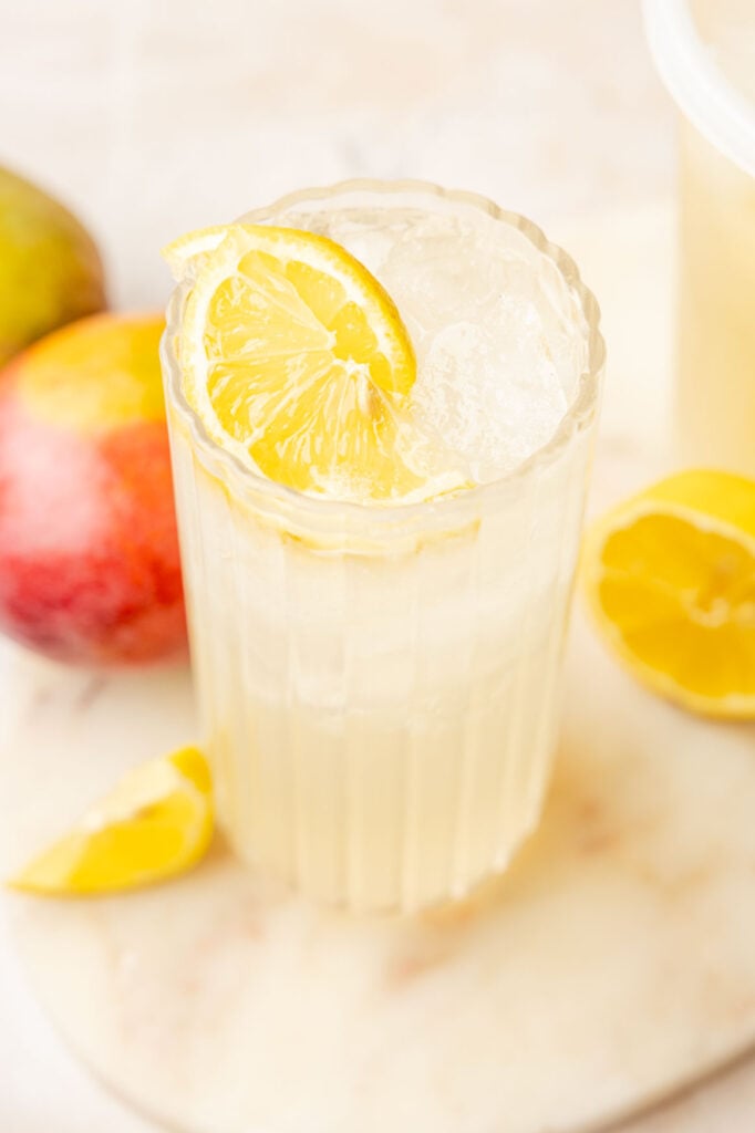 Mango Lemonade in a glass with lemons, inside and lemons and mangoes outside