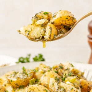 Spoon scooping French Potato Salad (Easy No Mayo Potato Salad) with some dressing dripping off the spoon.