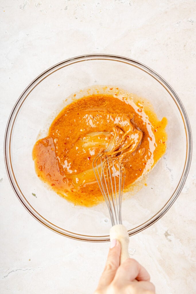 Whisking together the sesame sauce and a large mixing bowl.