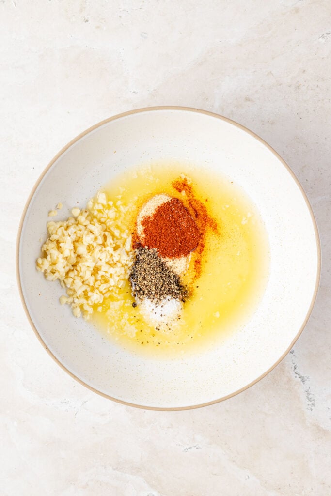 Melted butter, garlic, salt, pepper, and spices in a small bowl.