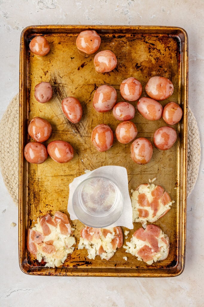 Demonstration of how to smash the potatoes with a cup on a sheet pan