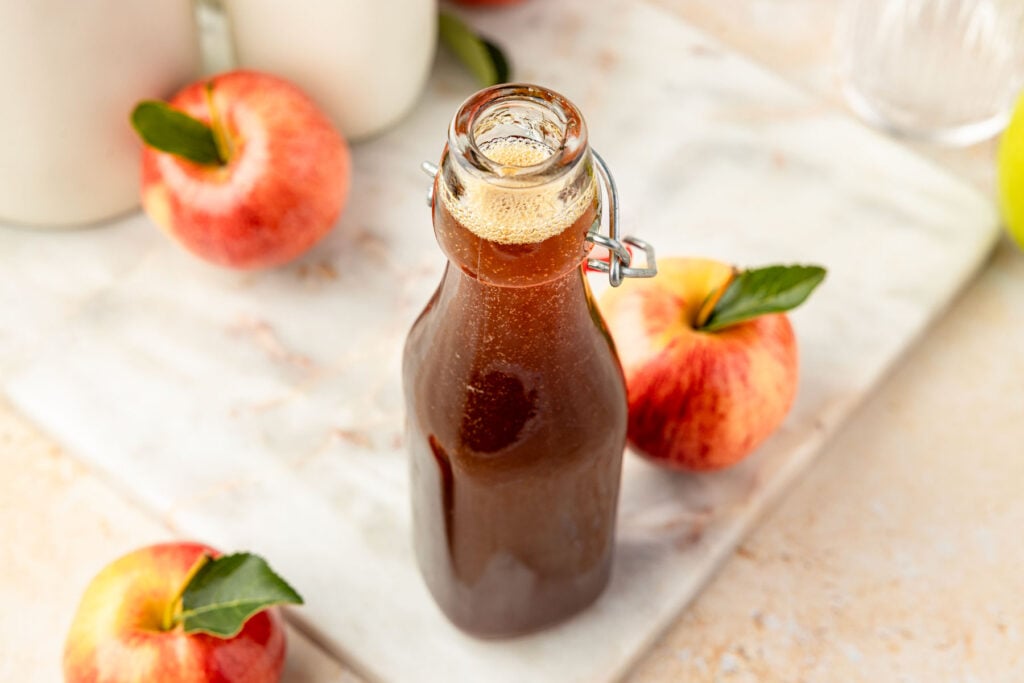 Apple brown sugar syrup in a jar with apples and coffee mugs around it