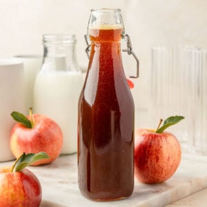 Apple brown sugar syrup in a jar with apples and coffee mugs around it.
