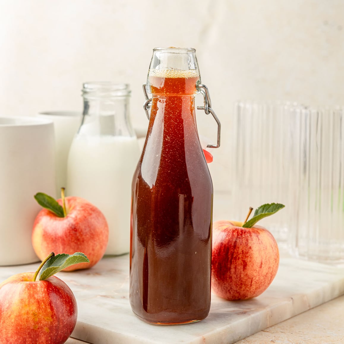 Apple brown sugar syrup in a jar with apples and coffee mugs around it