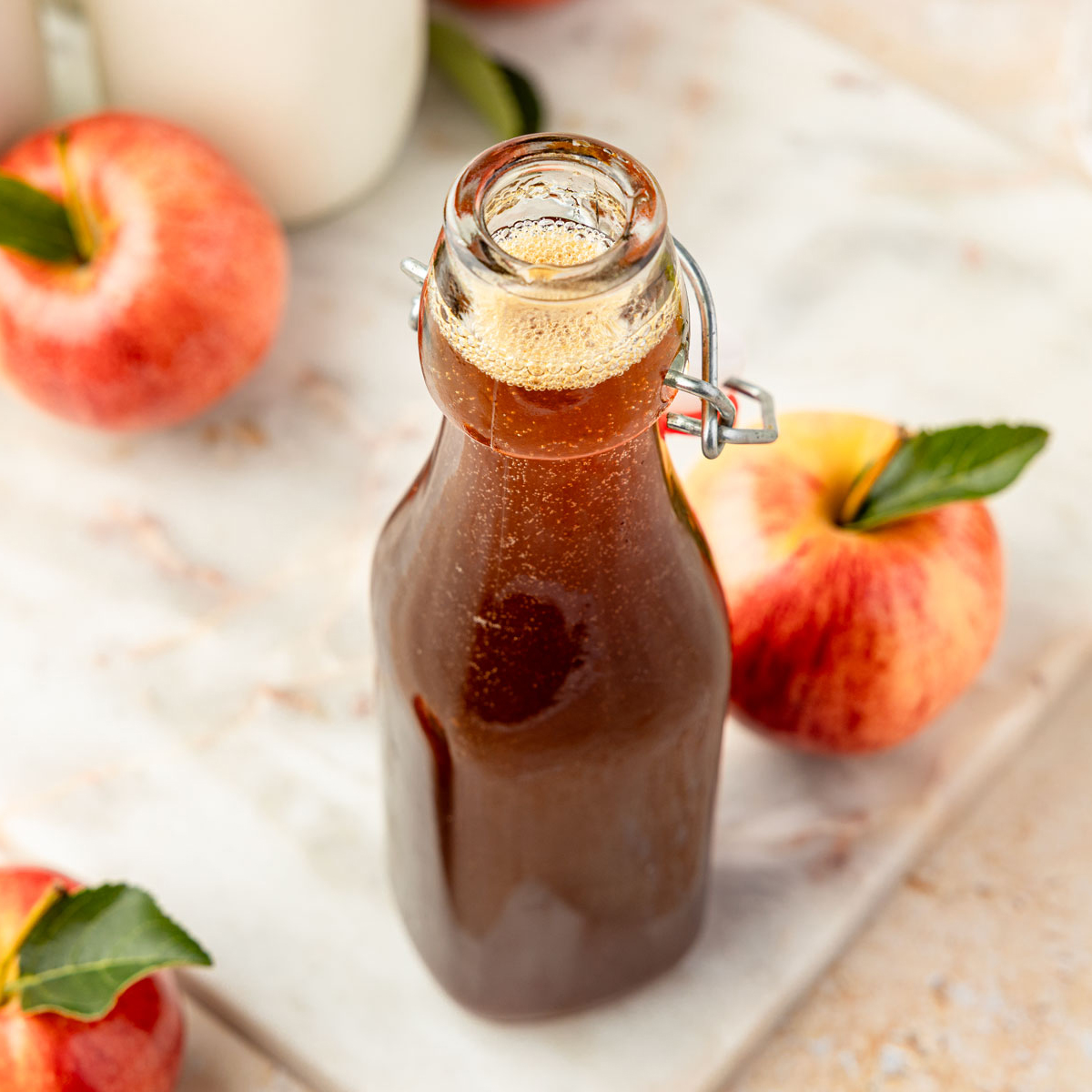 Apple brown sugar syrup in a jar with apples and coffee mugs around it