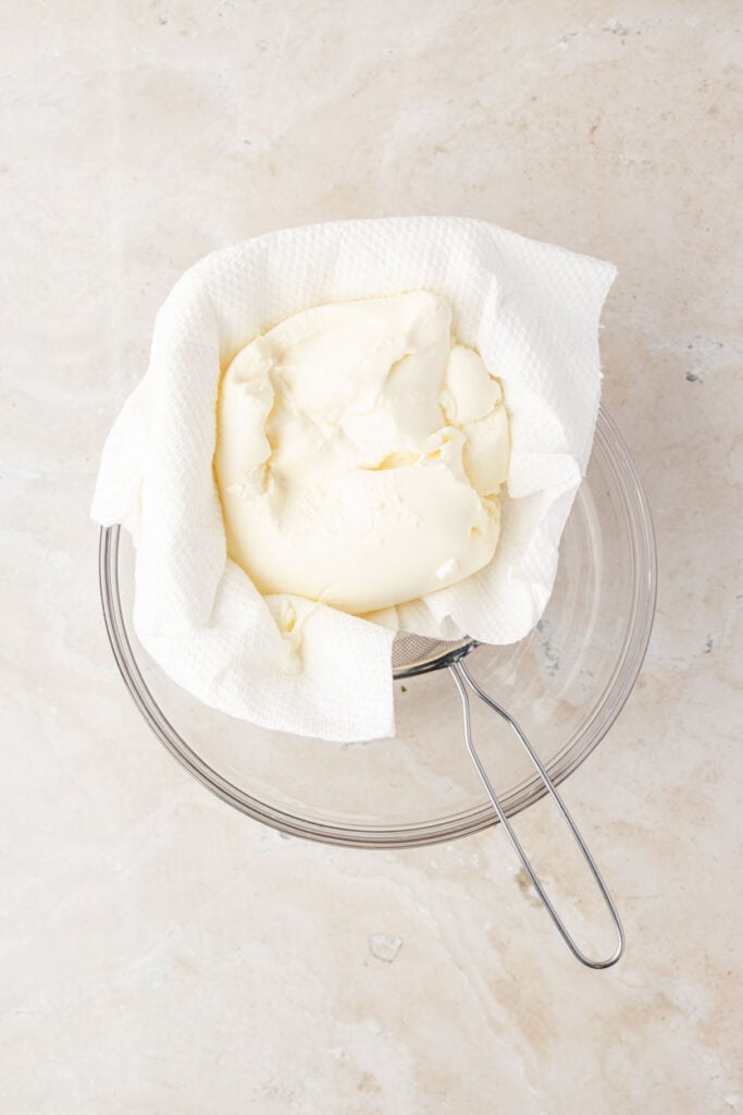 Ricotta cheese in a strainer over a bowl