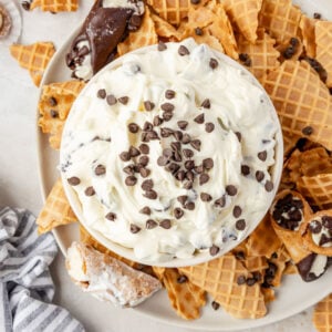 Cannoli Dip in a bowl with waffle cones and cannoli on a plate around it.