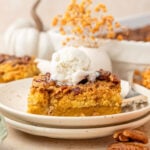 Pumpkin Crunch Cake on a plate topped with ice cream surrounded by pumpkins and pecans
