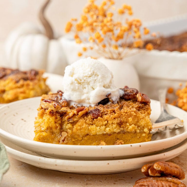 Pumpkin Crunch Cake on a plate topped with ice cream surrounded by pumpkins and pecans