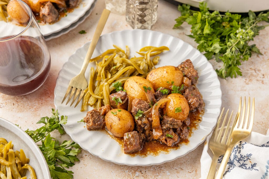 Slow Cooker Steak and Potatoes on a plate with herbs and wine.