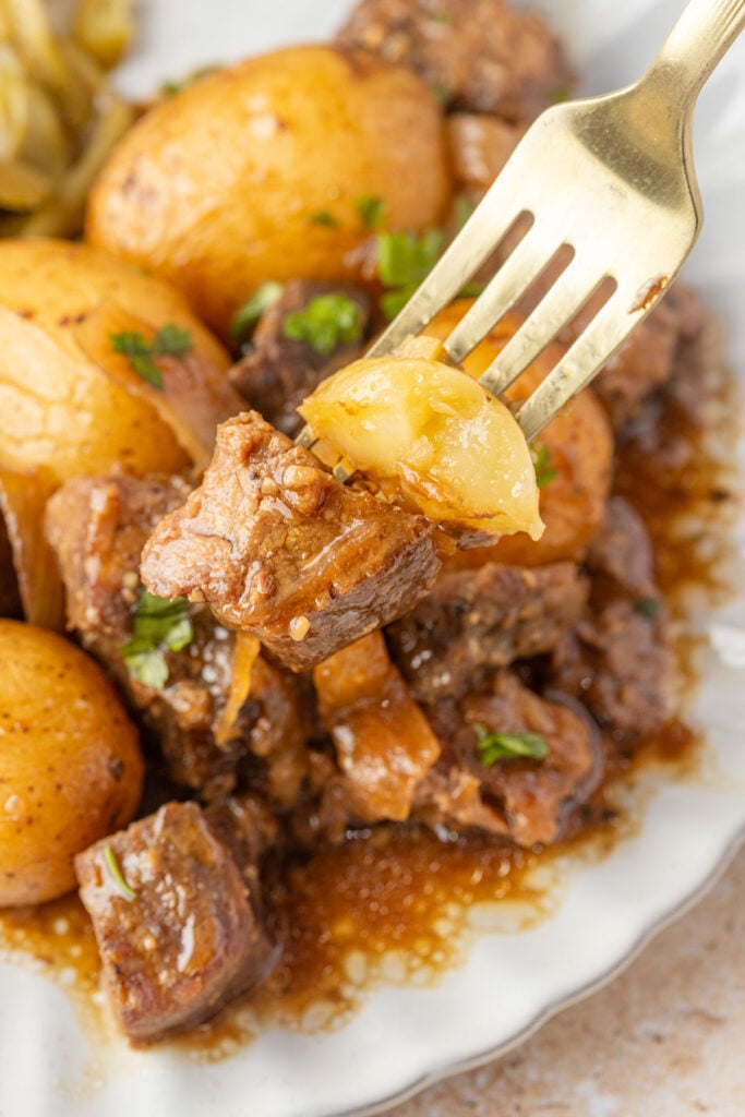 Slow Cooker Steak and Potatoes on a plate with a fork picking up steak bites.