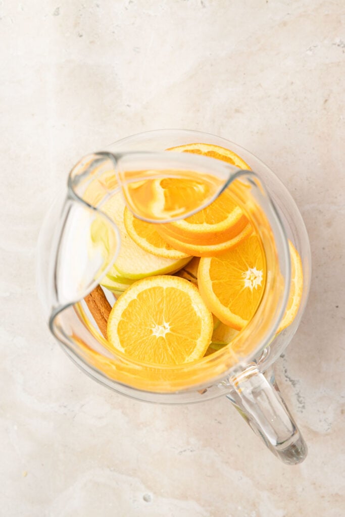 Orange slices, and apple slices in a pitcher.