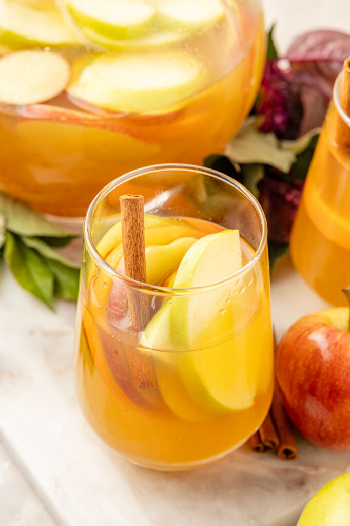 Apple Cider Sangria in a pitcher with fruit, flowers and leaves around it