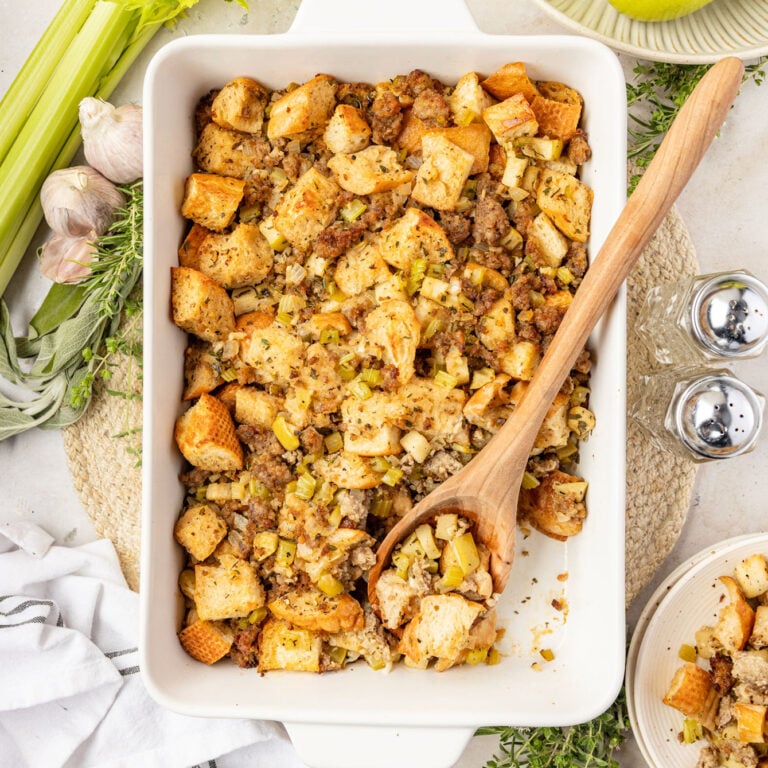 Apple Sausage Stuffing in a casserole pan with celery, garlic, apples, and herbs surrounding it.