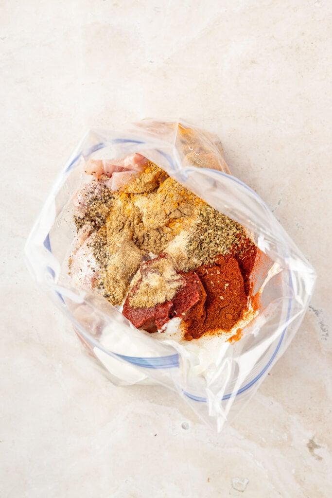 Raw chicken, spices, tomato paste, and Greek yogurt in a Ziploc bag