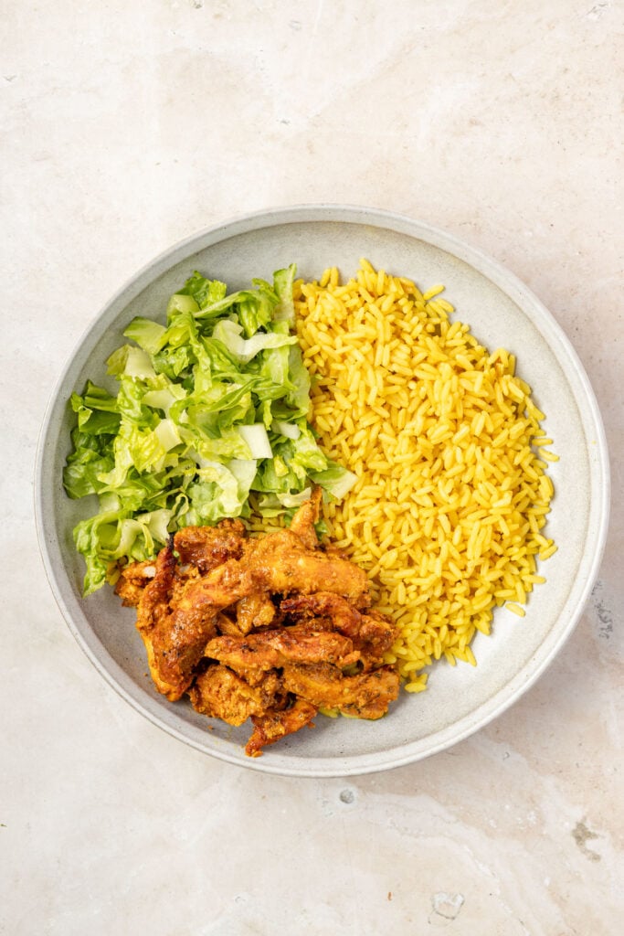 Rice and lettuce and Shawarma chicken in a bowl