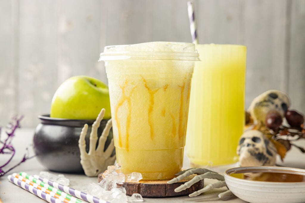 Homemade Alani Witch’s Brew in a cup with halloween decorations around it.
