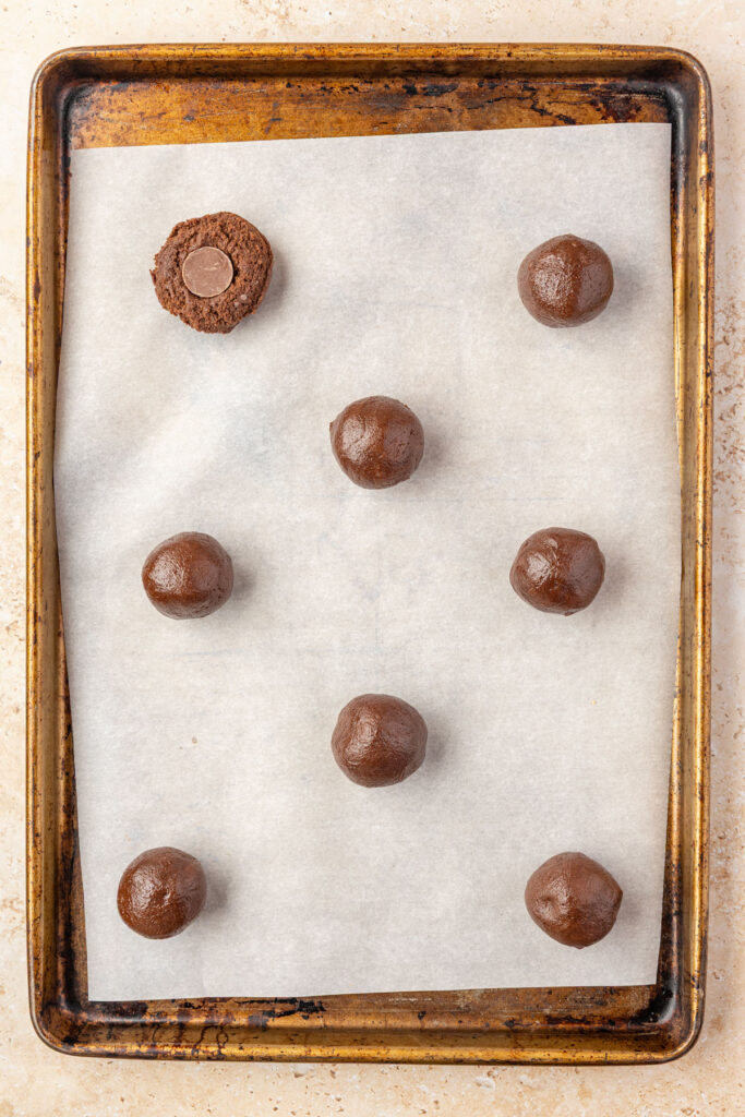 Raw Rolo Cookies on a cookie sheet, showing how you stop a rolo into the cookie.