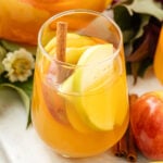 Apple Cider Sangria in a glass with fruit, flowers and leaves around it